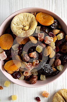 Dried fruits and nut mix in a pink bowl over white wooden surface top view. Overhead, from above, flat lay. Close-up