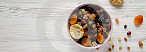 Dried fruits and nut mix in a pink bowl on a white wooden surface, top view. Overhead, from above, flat lay. Copy space