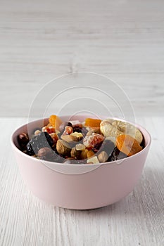 Dried fruits and nuts in a pink bowl over white wooden background, side view. Copy space