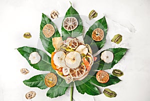 Dried fruits in a plate. Light concrete background on tropical leaf