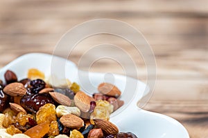 Dried fruits in white plate on wooden table, copy space for text. Mix of different varieties of nuts and berries, vitamins