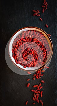 Dried goji berries in a bowl on dark background, top view