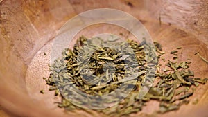 Dried green sencha tea leaves falling into a rustic wooden bowl