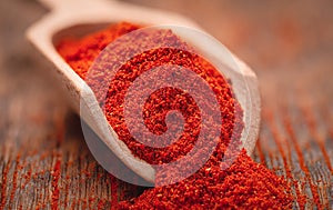 Dried ground paprika in a wooden scoop close up