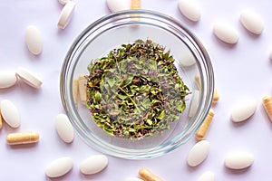 Dried herbs in a bowl on nutritional supplements pills background. Alternative herbal medicine, naturopathy and homeopathy