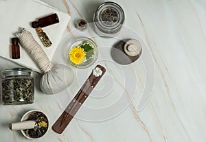 Dried herbs, small bottles of essential oils, mortar and pestle, massage herbal bag, fragrant stick on a marble background.