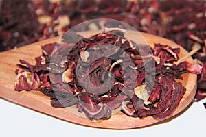 Dried hibiscus flowers (Hibiscus sabdariffa) for tea in a wooden spoon, resting on a white surface, blurred background..