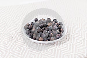 Dried juniper berries in a white bowl over fabric