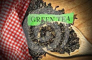 Dried leaves of green gunpowder tea on a wooden spoon