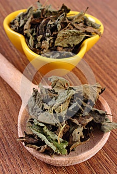 Dried lemon balm with spoon and bowl on wooden table, herbalism