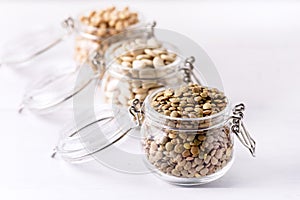 Dried Lentils Chickpeas White beans in Glass Jars on White Wooden Background