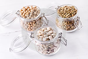 Dried Lentils Chickpeas White beans in Glass Jars on White Wooden Background Above Close Up