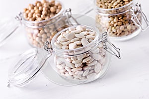 Dried Lentils Chickpeas White beans in Glass Jars on White Wooden Background Close Up