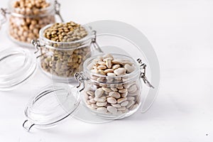 Dried Lentils Chickpeas White beans in Glass Jars on White Wooden Background Copy Space