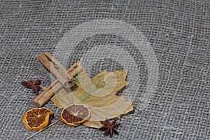 Dried maple leaves on a rough linen cloth. Nearby are cinnamon, dried orange slices and anise. Autumn still life