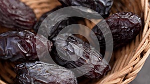 Dried medjool dates falling into a wooden rattan bowl closeup.