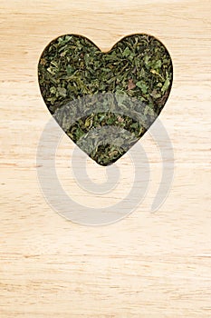 Dried nettle leaves heart shaped on wooden surface