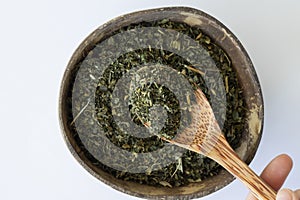 Dried nettle leaves for making medicinal tea in a wooden spoon on a beige background with a plate.