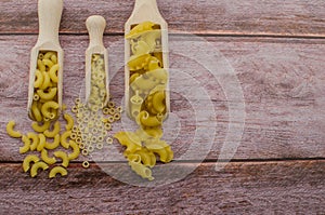 Dried pasta food selection in wooden spoons over old oak background