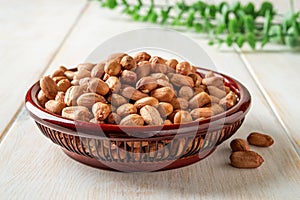 Dried peanut in a wooden bowl over white rustic table. Healhy vegetarian snack of whole peeled monkey nut. Raw groundnut seeds for