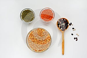 Dried peas, lentils and mung bean in bowls and beans in a wooden spoon on a white background