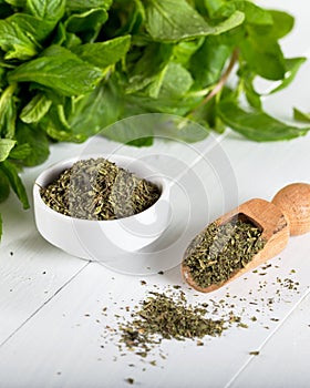 Dried peppermint in a white bowl and a bunch of fresh mint, on wooden background