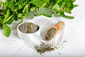 Dried peppermint in a white bowl and a bunch of fresh mint, on wooden background