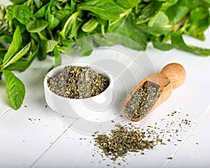 Dried peppermint in a white bowl and a bunch of fresh mint, on wooden background