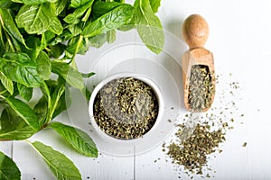 Dried peppermint in a white bowl and a bunch of fresh mint, on wooden background