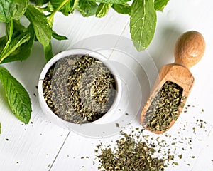 Dried peppermint in a white bowl and a bunch of fresh mint, on wooden background