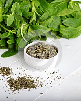 Dried peppermint in a white bowl and a bunch of fresh mint, on wooden background