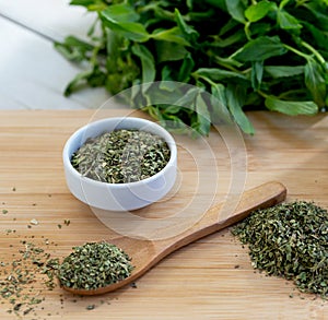 Dried peppermint in a white bowl and a bunch of fresh mint, on wooden background