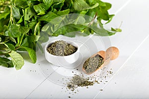 Dried peppermint in a white bowl and a bunch of fresh mint, on wooden background. Food background