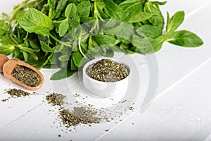 Dried peppermint in a white bowl and a bunch of fresh mint, on wooden background. Food background