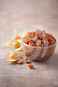 Dried physalis in wooden bowl and fresh berries on wood textured background. Copy space. Superfood, vegan, vegetarian food concept