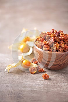 Dried physalis in wooden bowl and fresh berries on wood textured background. Copy space. Superfood, vegan, vegetarian food concept