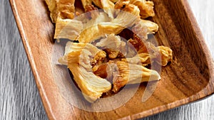 Dried pineapple pieces in wooden rustic dish. Dehydrated sliced juicy tropical fruit.