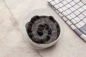 Dried plums in a white bowl isolated on marble background