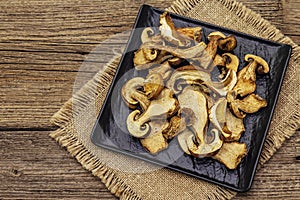 Dried porcini mushrooms. Traditional ingredient for cooking healthy food. Black ceramic plate, sackcloth napkin, old wooden boards