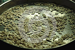 Dried pumpkin seeds in a round metal pan. Selective soft focus, close-up.