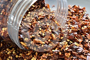 Dried red chilli flakes spilling out of a plastic jar.