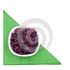 Dried red cranberries in a bowl on green serviette, napkin isolated on white, top view.