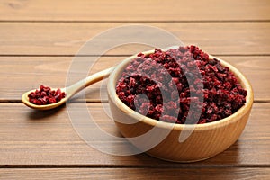 Dried red currants in bowl and spoon on wooden table