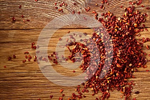 Dried red hot chilly flakes on rustic wooden background, top view, close-up, macro, selective focus.