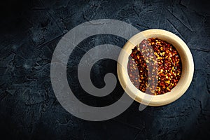 Dried red pepper flakes in a wooden bowl. Chili pepper flakes on a dark background.