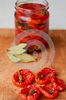 Dried red tomatoes with spices on wooden board close up. Jar with many dried tomatoes on the blurred background