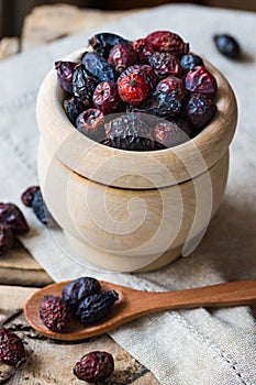 Dried rose hip berries in wood bowl, spoon, scattered on linen towel, health concept, natural medicine