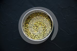 Dried rosemary spice in a metal box on a black background