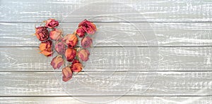 Dried roses in shape of heart on background of wooden boards painted in gray.Concept of idea of ageless love.Copy space