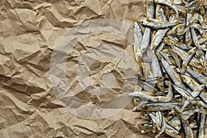 Dried salted sardelle fish on crumpled parchment paper background